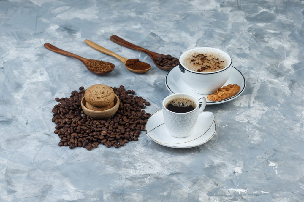 Set of cookies, coffee beans, grinded coffee and coffee in cups on a grungy grey background. high angle view. espresso and coffee